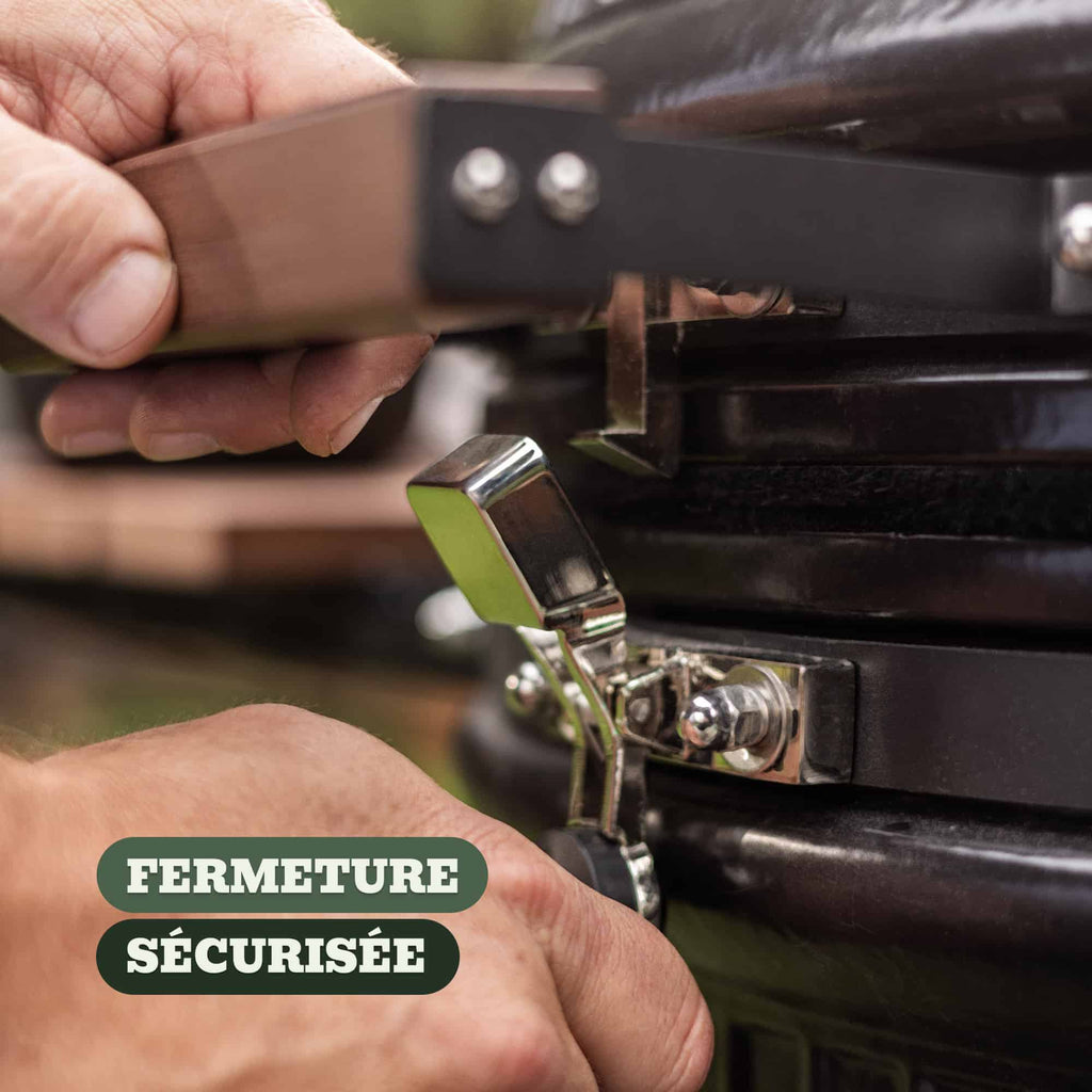 Gros plan sur la fermeture sécurisée d’un barbecue Kamado, montrant une main actionnant un loquet métallique robuste pour maintenir le couvercle bien scellé.